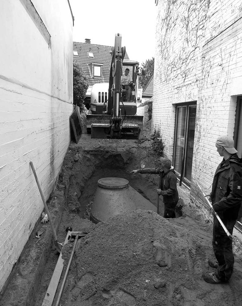 Ein Bagger legt den Raum zwischen zwei Gebäudeteilen frei.