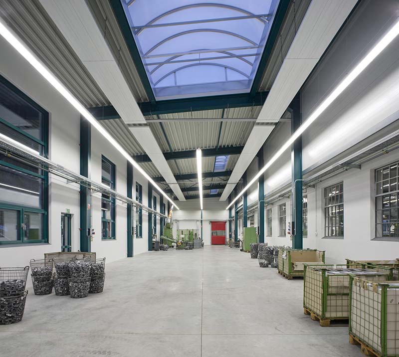 Innenraum einer Industriehalle mit stützenfreiem Grundriss und großen Fenstern und Oberlichtern.