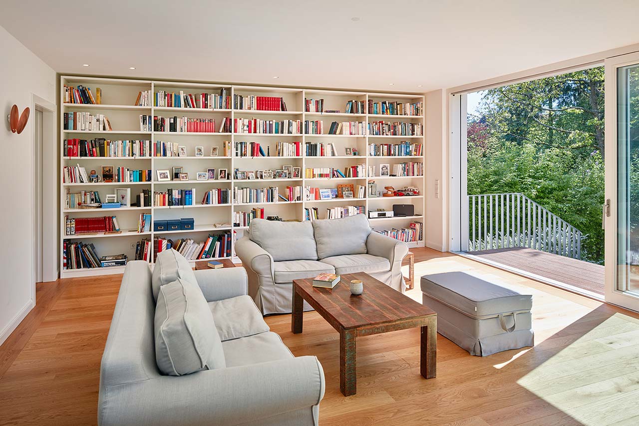 Wohnraum mit Bibliothek und wandgroßer Fensterschiebetür.
