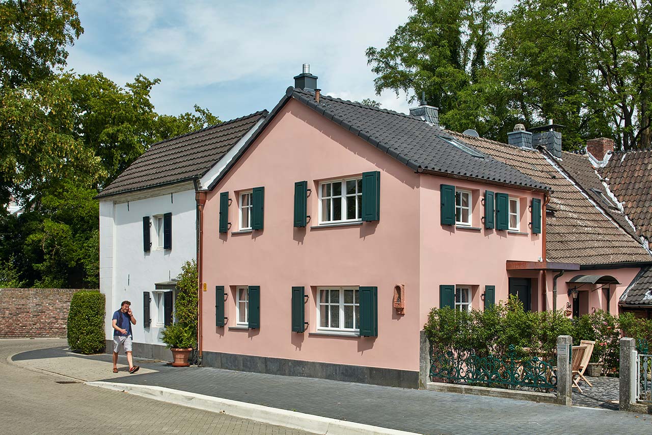 Ein kleines altes Haus mit rosa Fassade und dunkelgrünen Fensterläden nach der umfangreichen Sanierung.