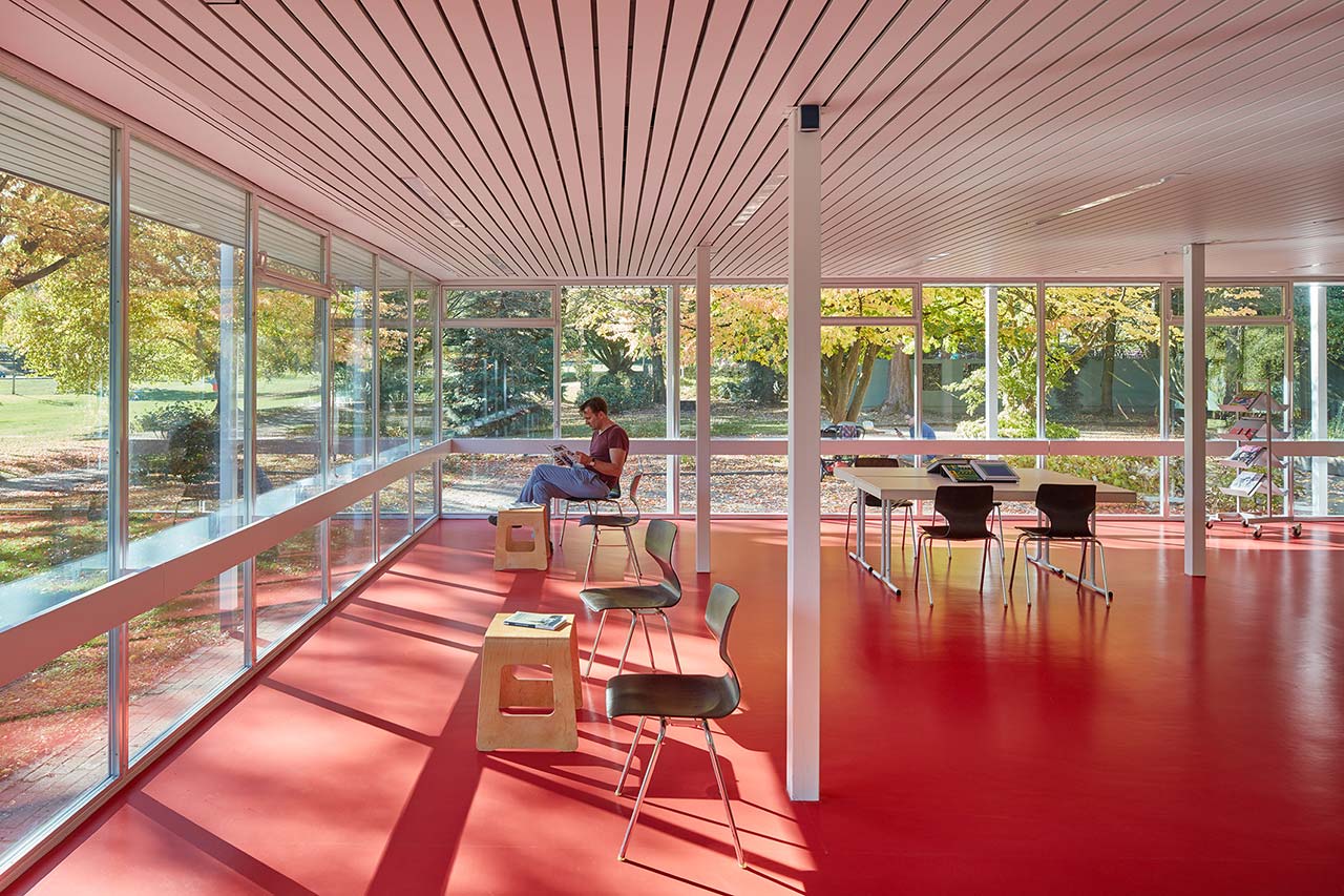 Innenraum des vollverglasten Lesepavillons mit rotem Fußboden.