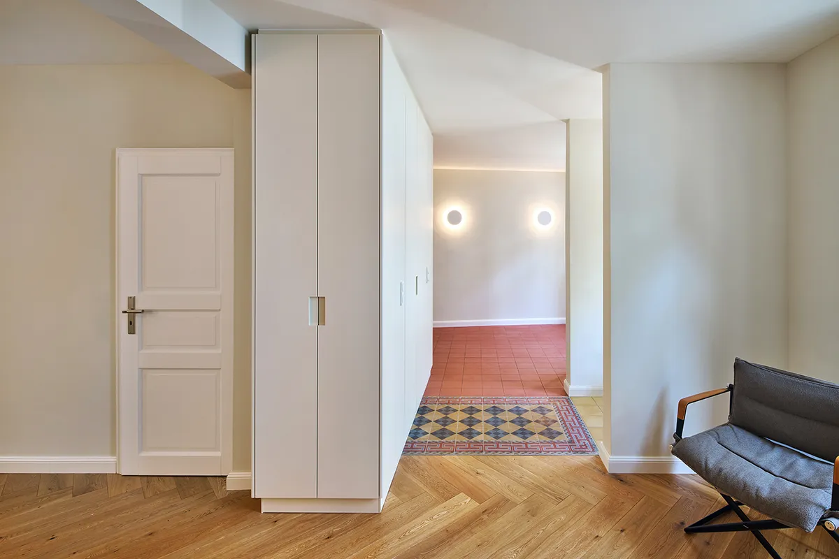 Sanierter Innenraum mit Einbauschrank, Holzboden im Fischgrätmuster und Blick in angrenzenden Raum mit Fliesenboden.