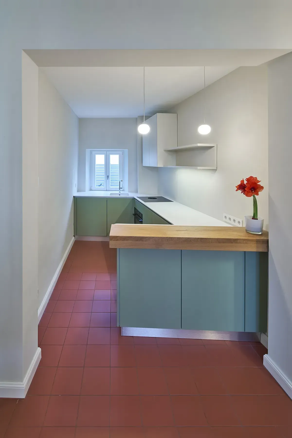Sanierte Küche mit Einbauten in Grün, Arbeitsplatte aus Holz, weißen Oberflächen und rotem Fliesenboden.
