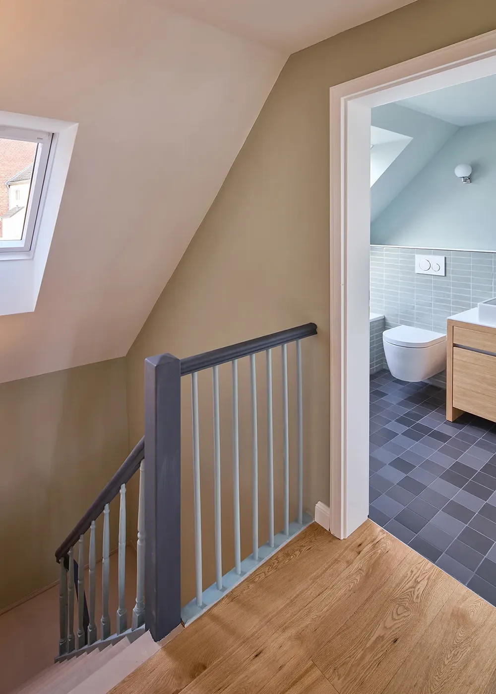 Sanierter Flur im Dachgeschoss mit Treppenbrüstung, Holzboden und Zugang zum Badezimmer.