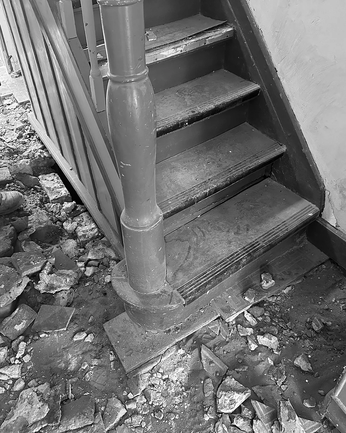 Treppenbereich während der Sanierung mit freigelegten Stufen, historischem Geländer und Bauschutt im Eingangsbereich.