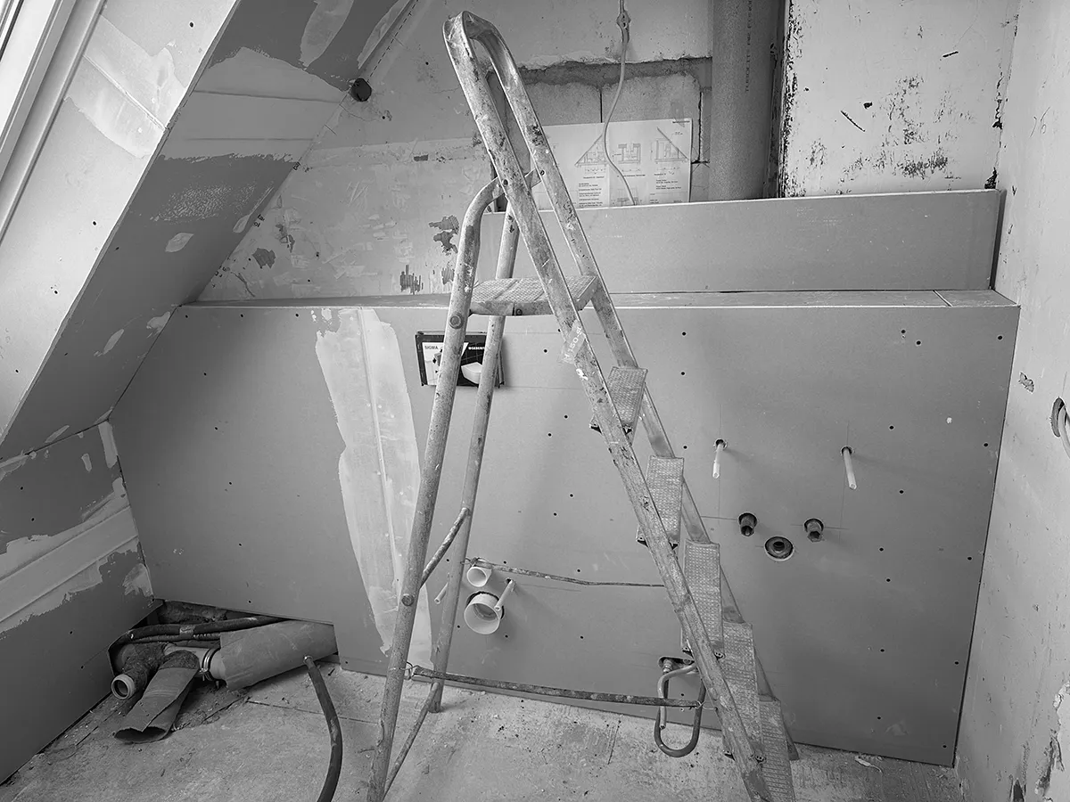 Innenraum im Dachgeschoss während der Sanierung mit Trockenbauverkleidung, sichtbaren Installationsanschlüssen und Leiter.