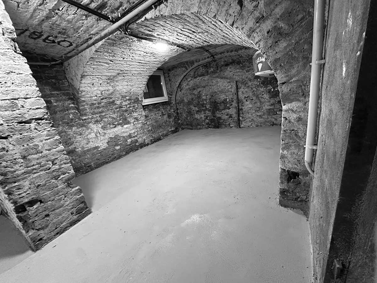 Gewölbekeller bei Sanierungsarbeiten mit freigelegtem Mauerwerk, erneuertem Boden und sichtbaren Leitungsführungen.