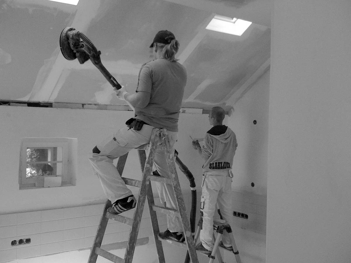 Arbeiter schleifen die Rigipsplatten an einer Dachschräge.